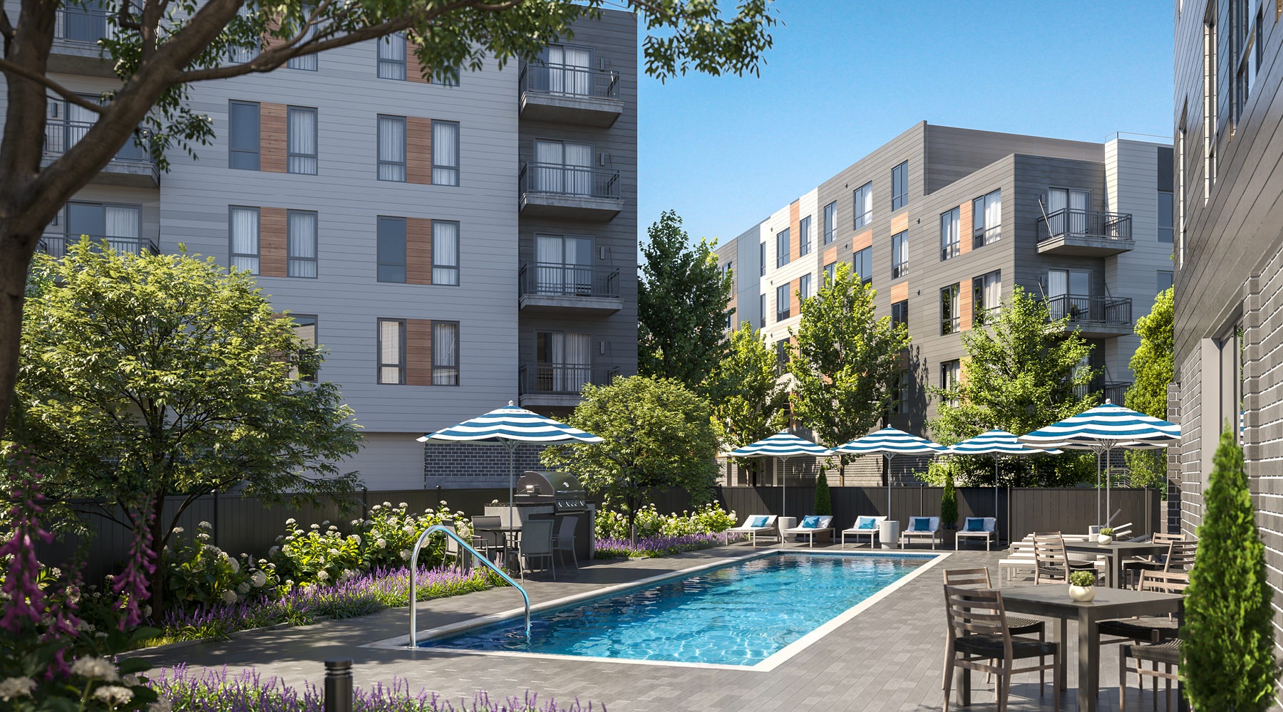 The pool area at Lore Apartments in Salem, MA, featuring lounge chairs, umbrellas, and a view of the apartment exteriors.